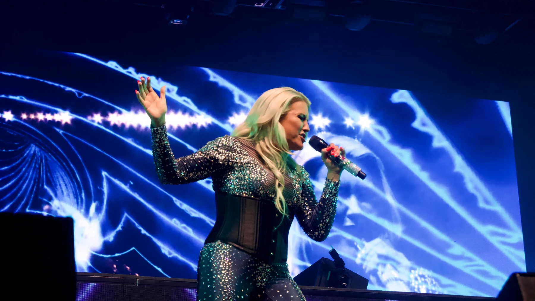 Cascada singing live at Motorpoint Arena in a sparkling outfit, in front of a giant blue LED screen