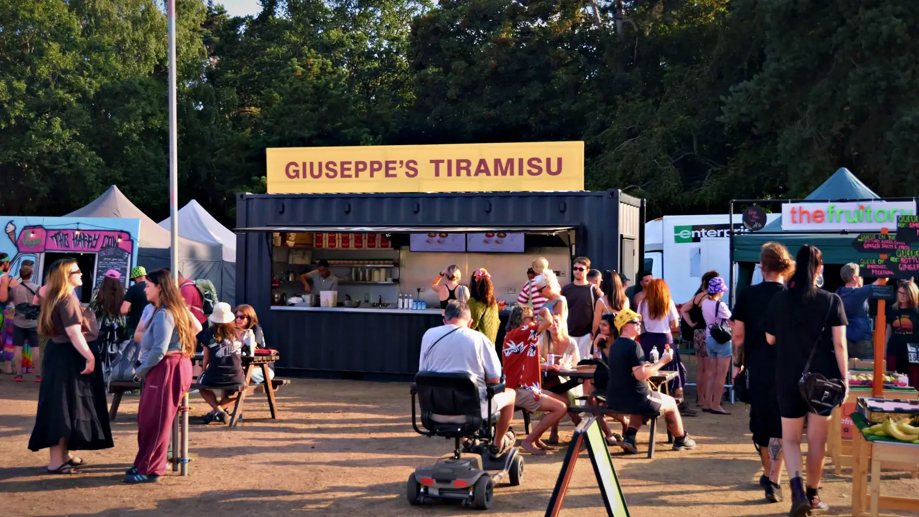Festival goers outside a BoxKitchen container unit trading as Giuseppe's Tiramisu at Vegan Camp Out on a sunny evening