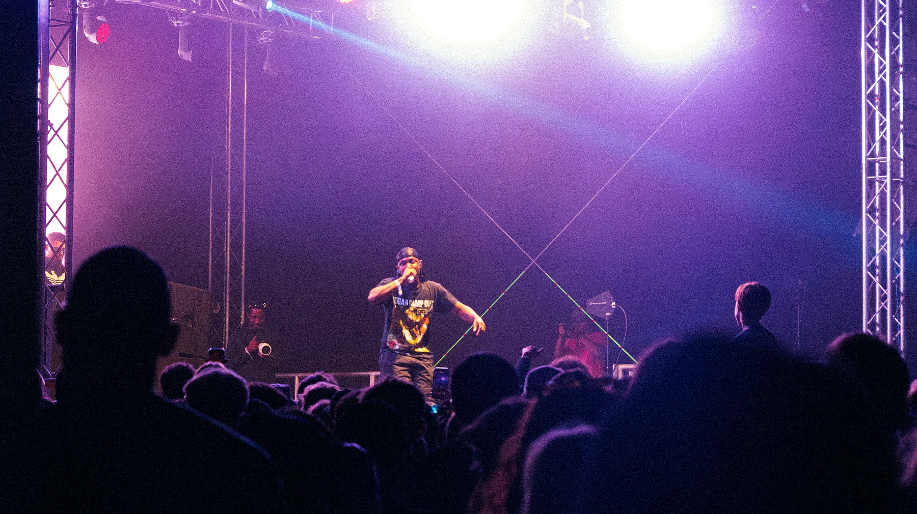 JME performing live on the main stage at Vegan Camp Out under purple lights, the crowd in silhouette