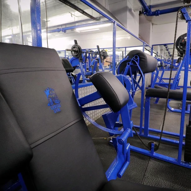 Black padded machine seat embossed with the Castle Gym logo, with blue machines stretching back across the floor