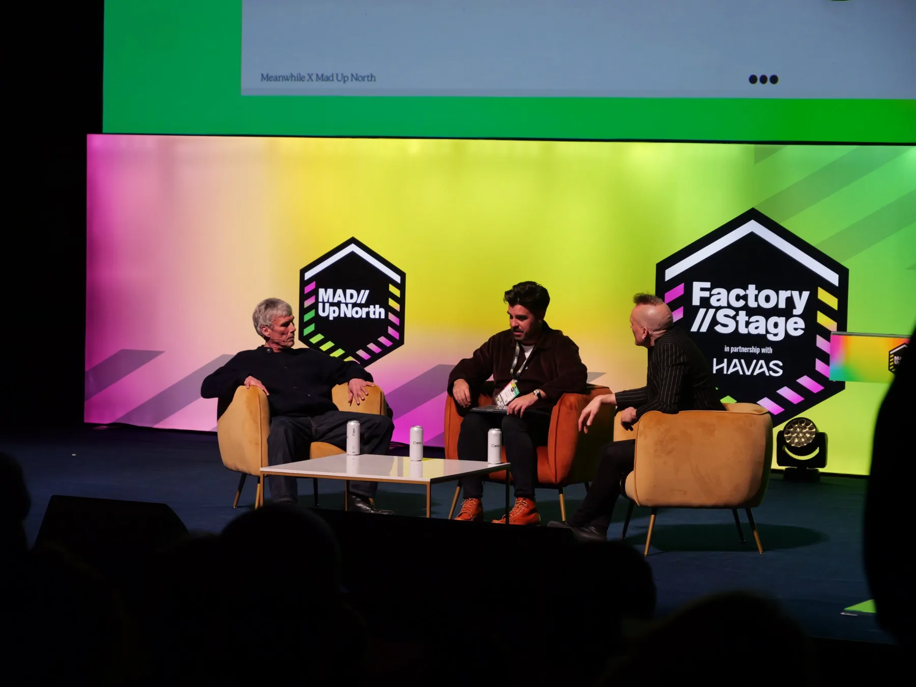 Three panellists in velvet armchairs on the Factory Stage at MAD//Fest Up North, under a pink and lime backdrop