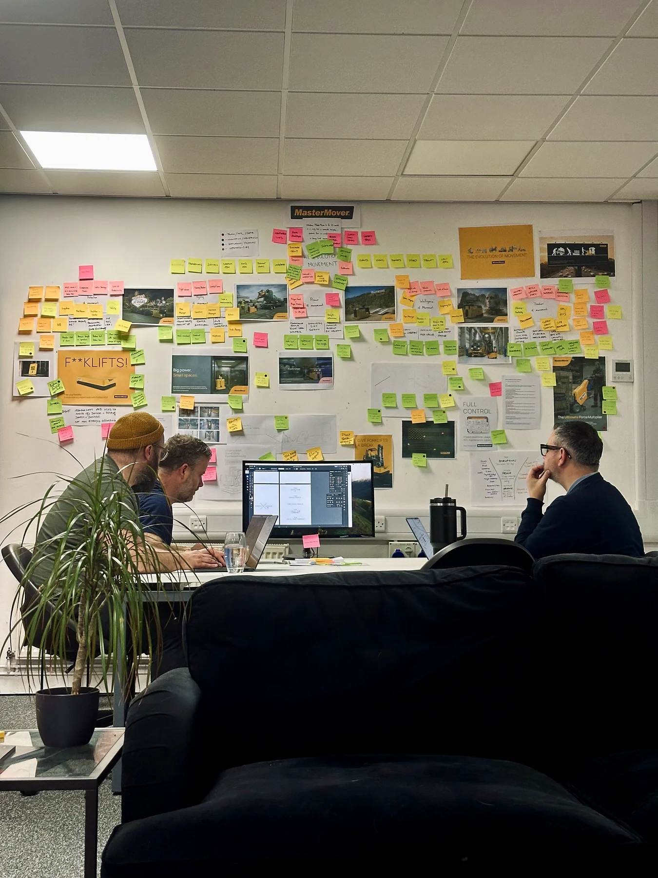 The Create Inc team at work in the studio, with a wall of sticky notes and planning sheets behind them