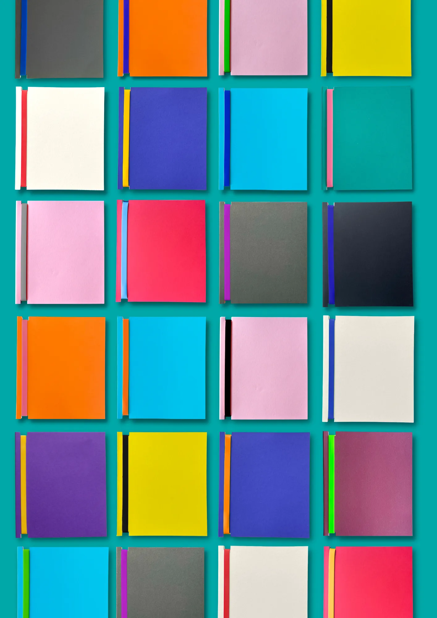Grid of 24 Dizzy Ink Book for Life refillable notebooks in different colourways, shot as a flat lay on a teal background