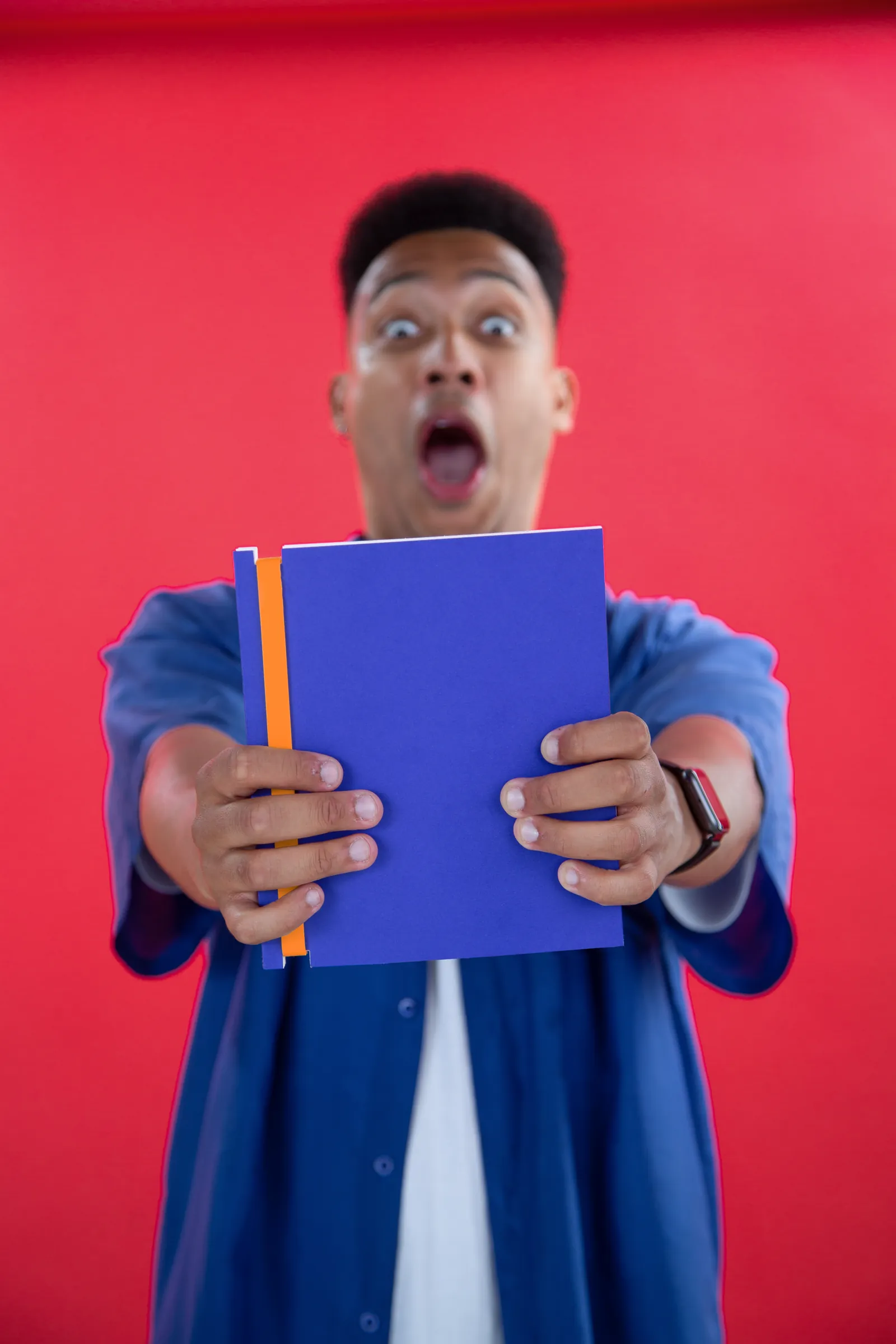 Surprised man holding a purple Book for Life notebook with an orange spine towards the camera against a bright red backdrop
