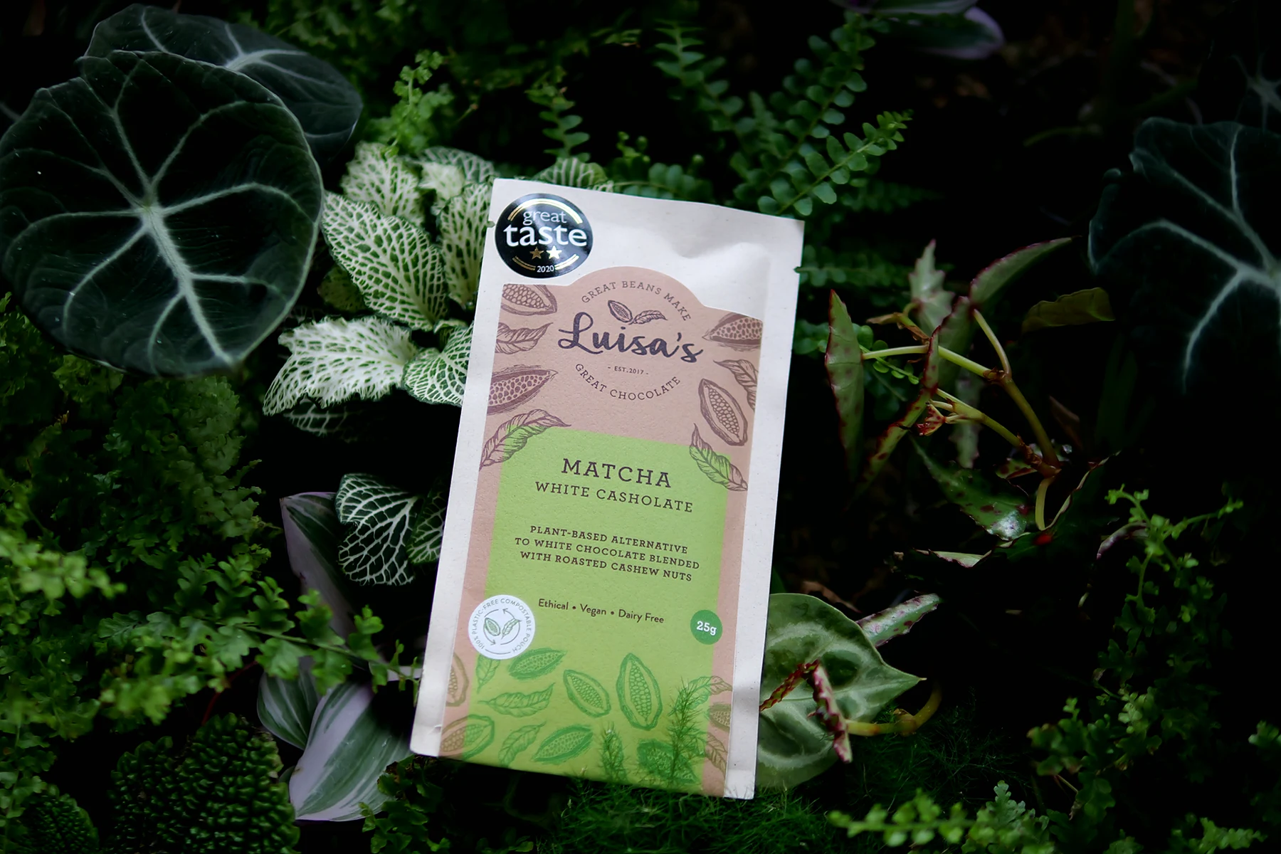 Luisa's Vegan Chocolates Matcha White Casholate bar in its compostable pouch with a Great Taste 2020 award, styled among tropical leaves, ferns and nerve plants