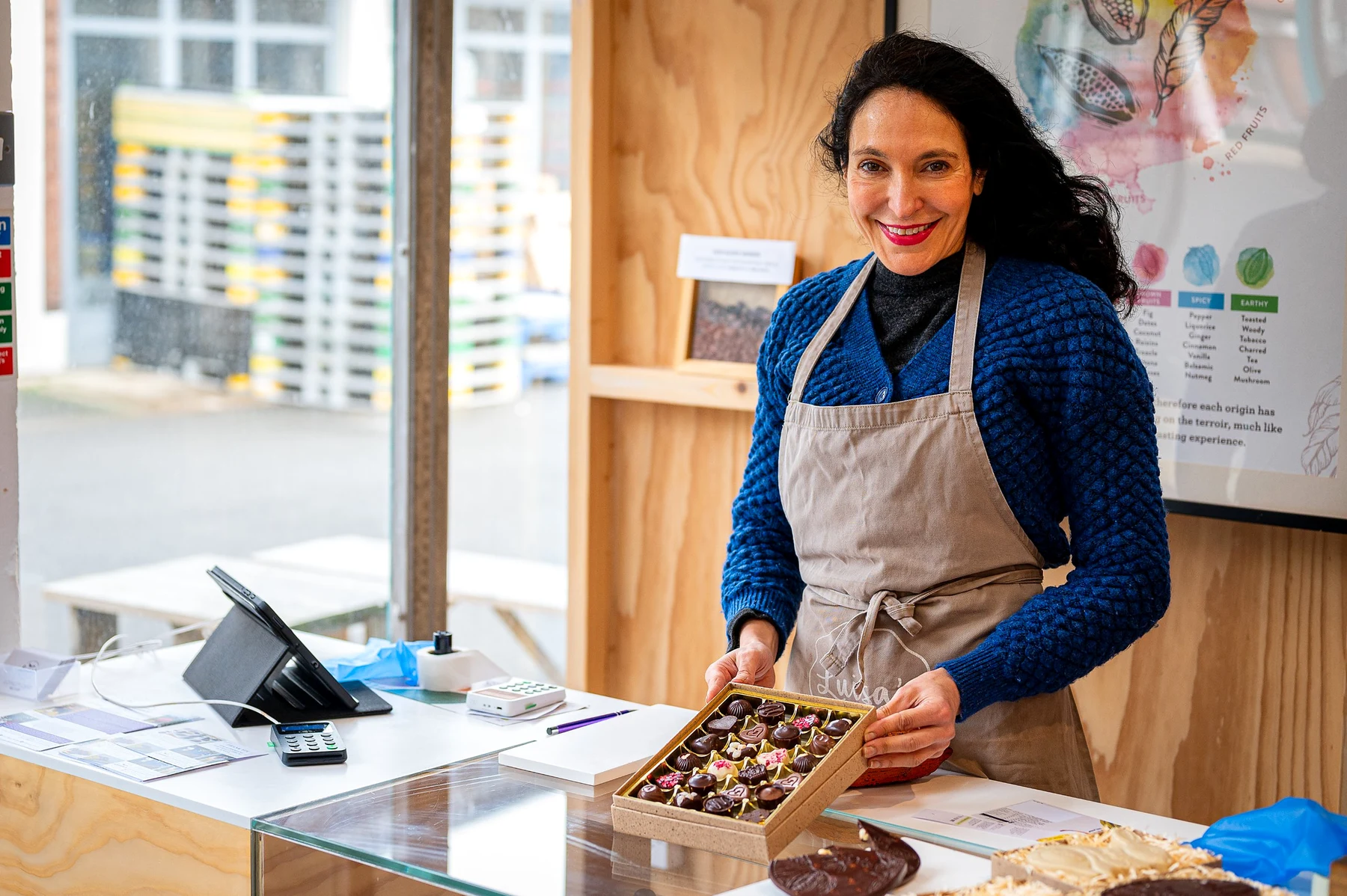 Smiling chocolatier in a Luisa's apron holding out a box of handmade vegan chocolates behind the shop counter