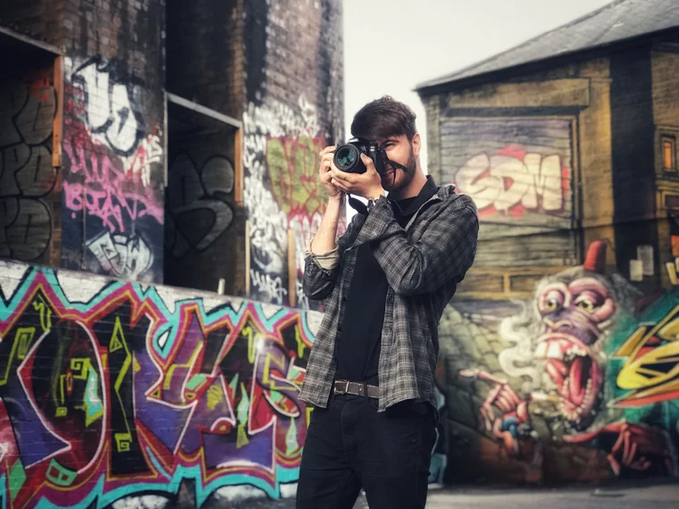 Luke Gray with his camera in front of a graffiti wall