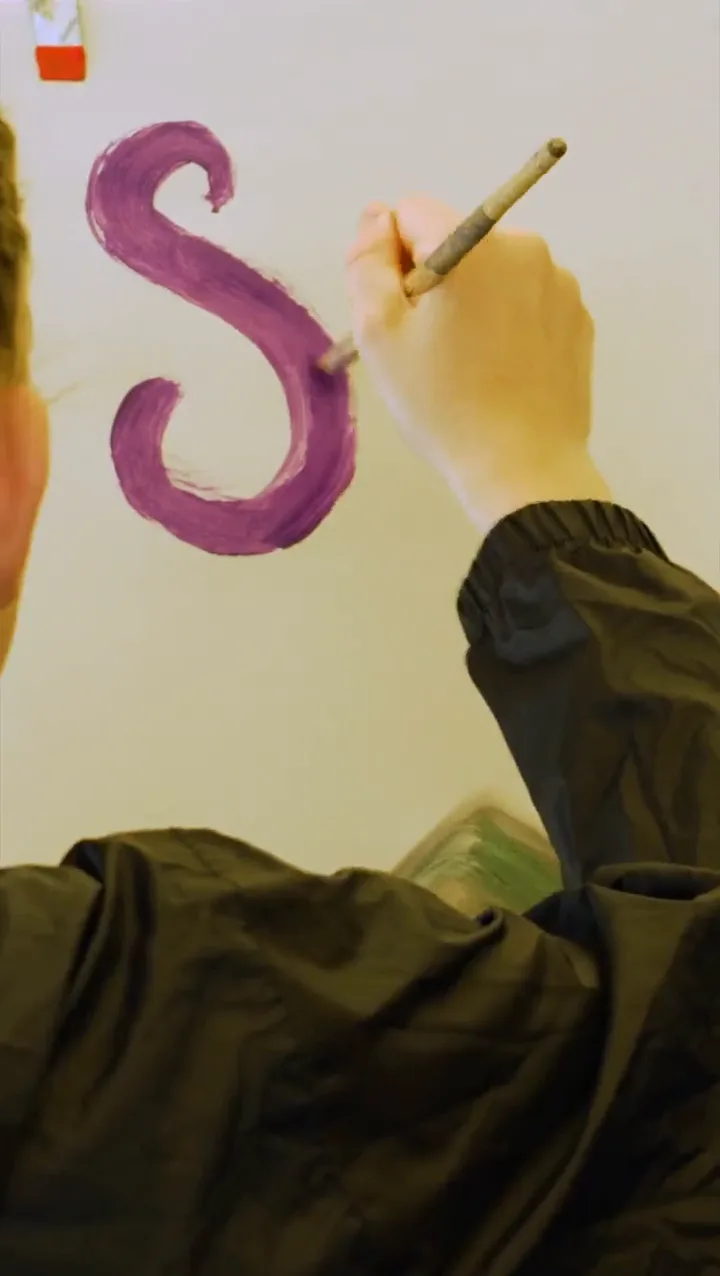 A hand painting the purple S of the Solfest logo with a brush