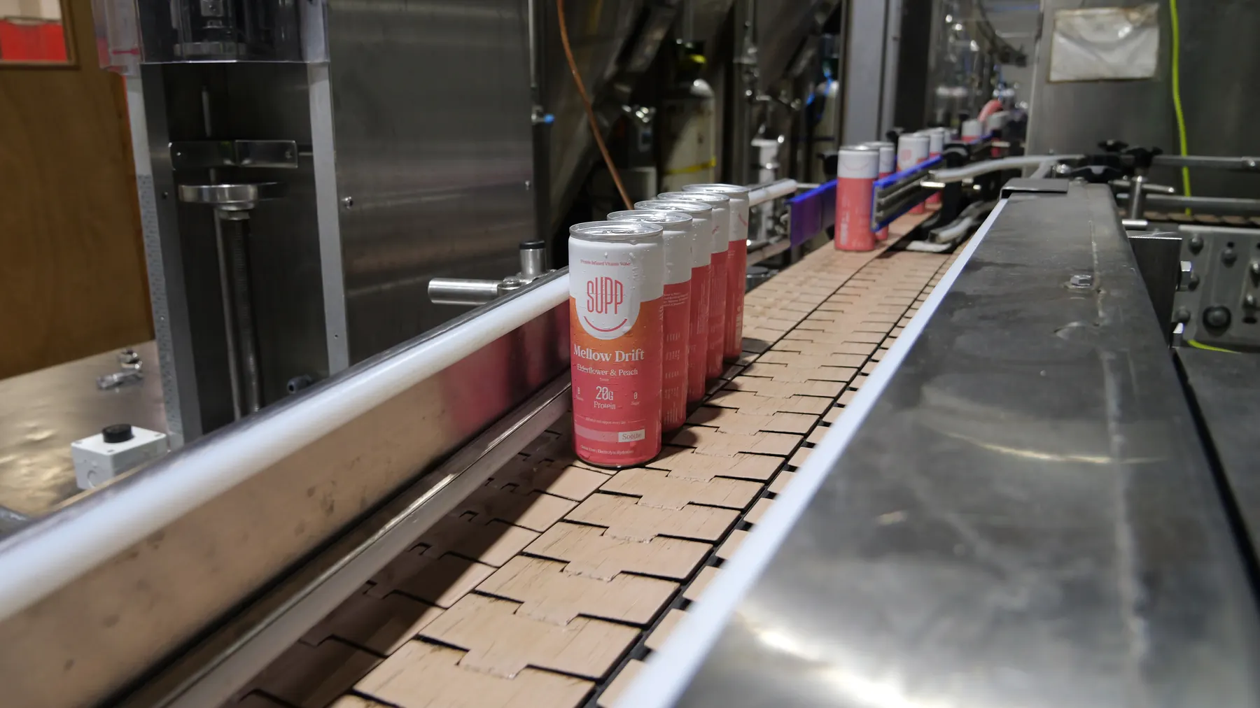 Pink flavour Supp cans travelling in a line along a stainless steel conveyor