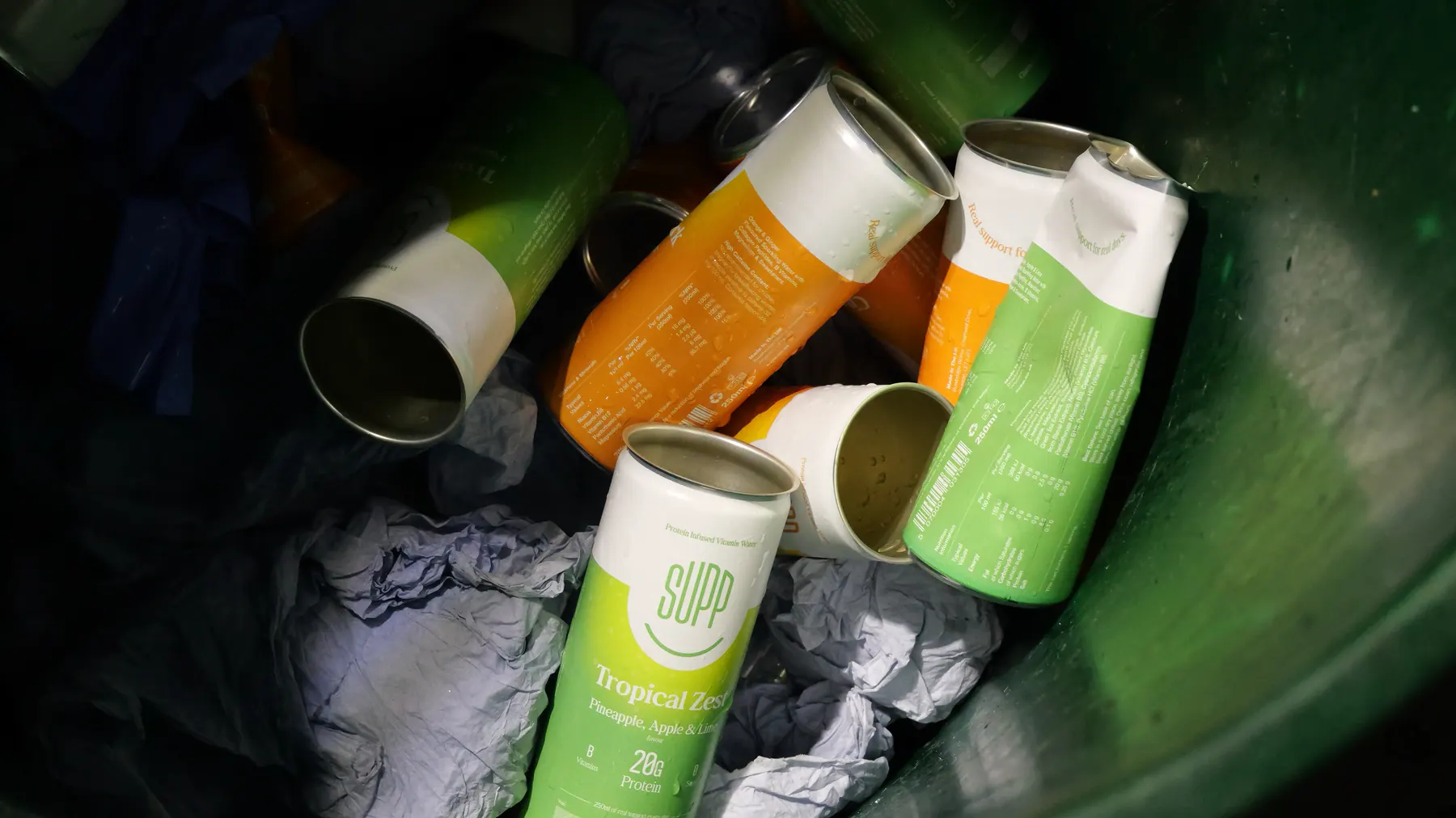 Rejected Supp cans in orange, green and white flavours in a recycling bin