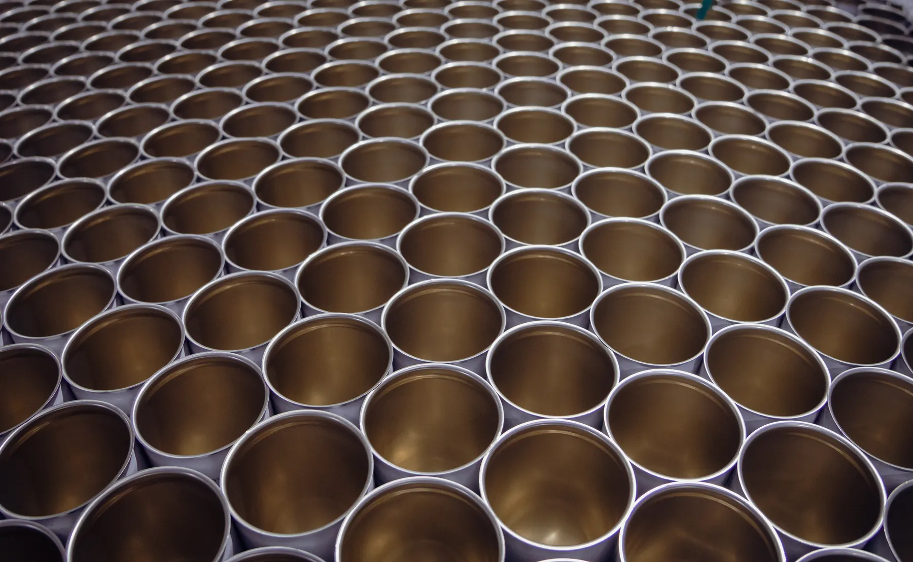 Pattern of hundreds of empty open cans glowing gold under factory light