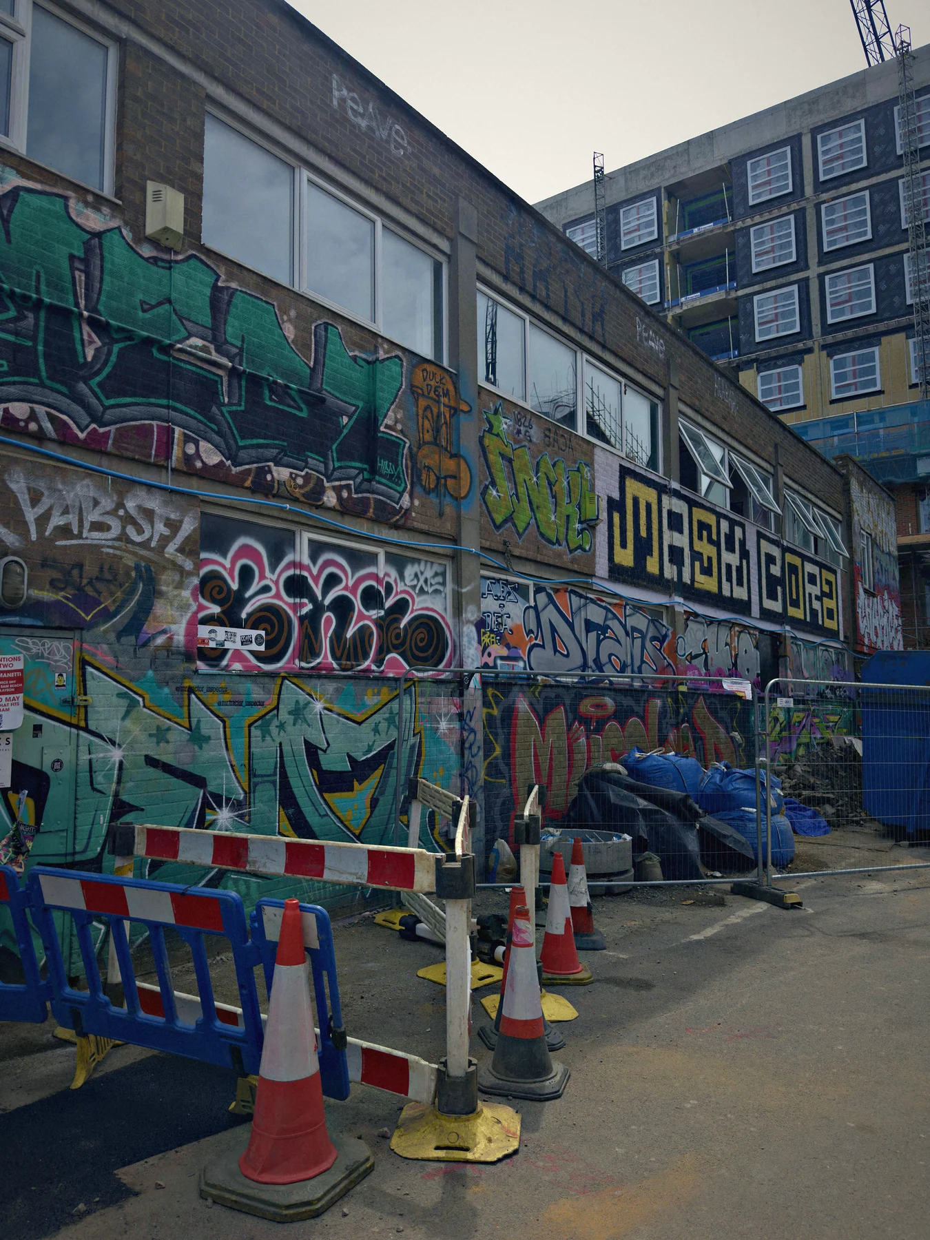 A graffiti covered street with hoardings, traffic cones and old brick buildings in London