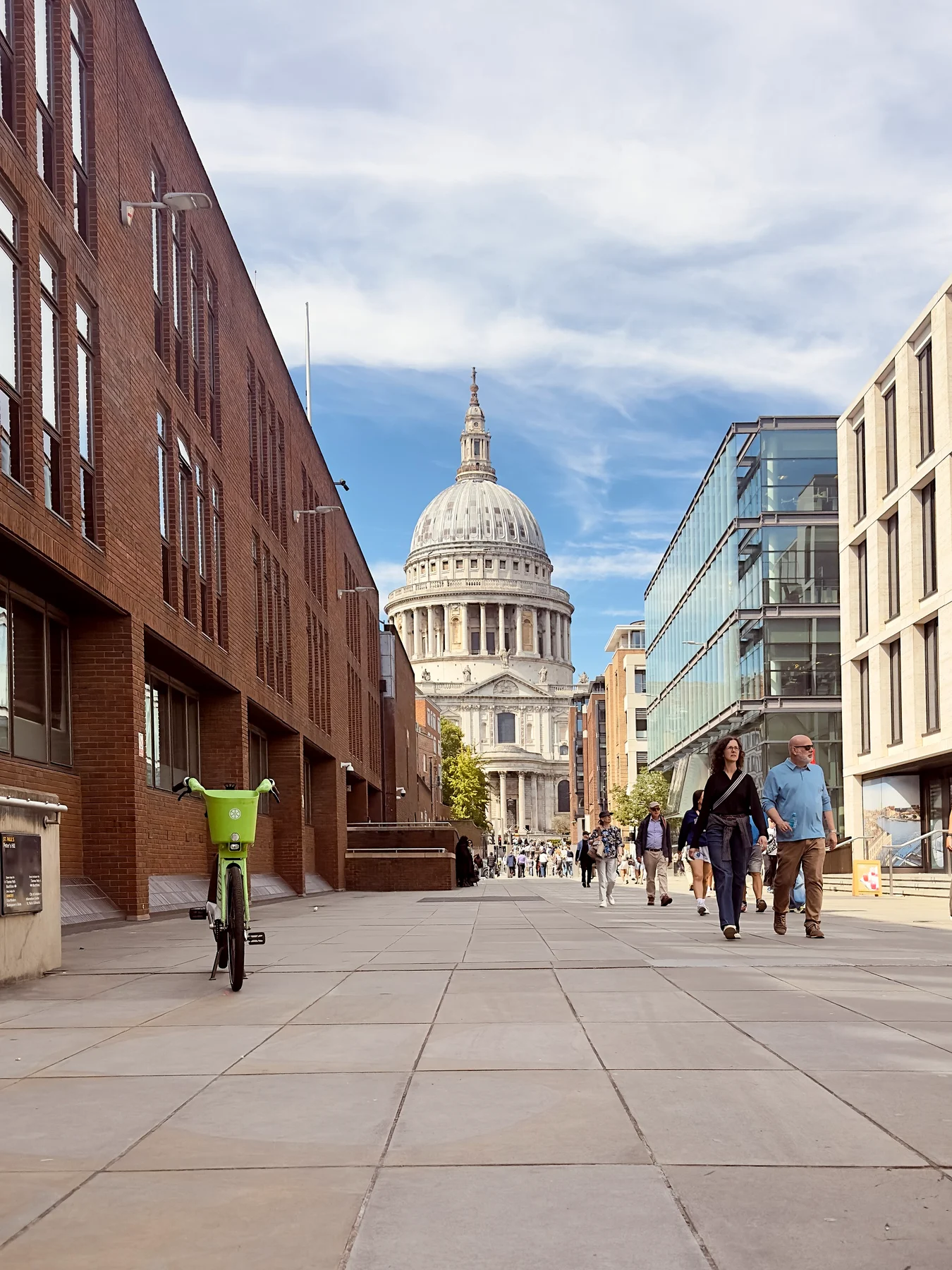 The dome of St Paul's Cathedral at the end of a London street, with people walking and cycling towards it
